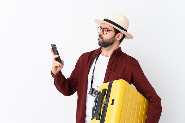 Homme homme voyageur avec barbe tenant une valise sur la pensée de mur blanc isolé et l'envoi d'un message