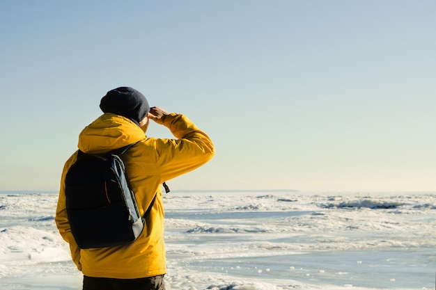 Homme en imperméable jaune avec sac à dos debout sur la mer gelée et à loin