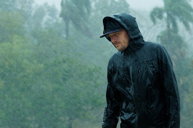 Homme en imperméable sous de fortes pluies tropicales.