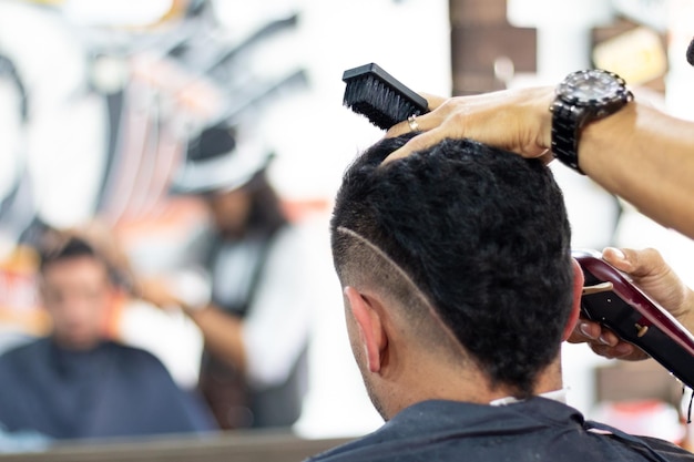 Homme inconnu assis dans un salon de coiffure devant un miroir tout en étant soigné.