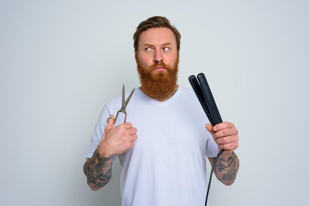 L'homme indécis avec des ciseaux et un lisseur est prêt à travailler avec des cheveux