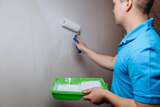 Un homme indépendant effectue des réparations dans un appartement en apprêtant les murs tenant un bac de peinture à la main Concept de bricolage