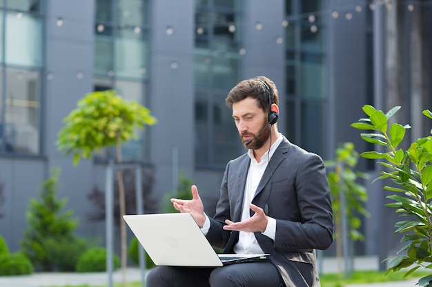 Un homme indépendant qui réussit effectue une consultation en ligne utilise un casque avec un microphone et un ordinateur portable pour la communication vidéo