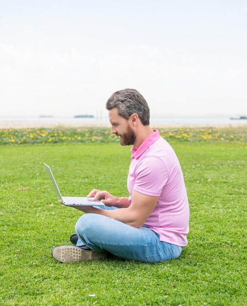 Un homme indépendant souriant publie un blog en ligne assis sur un réseau d'herbe