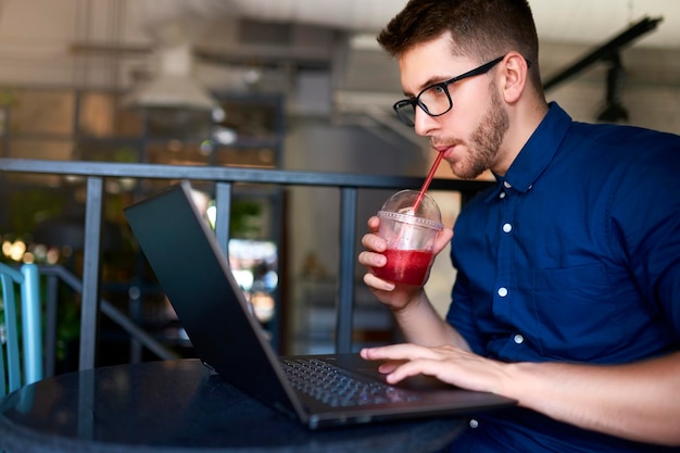 L'homme indépendant avec une tasse en plastique de boisson fraîche à la main travaille avec un homme d'affaires d'ordinateur portable dans des verres