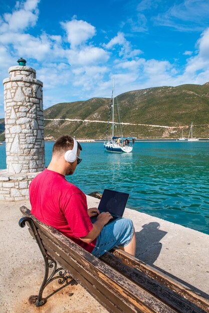 Homme indépendant travaillant sur ordinateur portable au banc du port de la ville en été