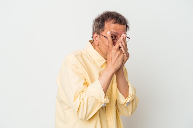 Homme indien d'âge moyen isolé sur fond blanc clignote à travers les doigts effrayé et nerveux.