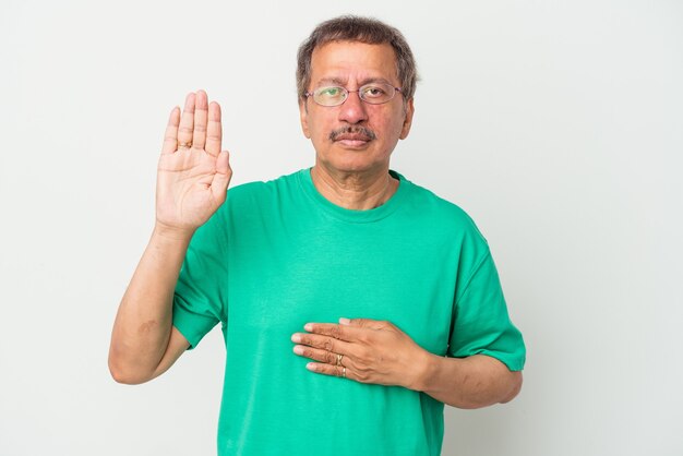 Homme indien d'âge moyen isolé sur fond blanc prêtant serment, mettant la main sur la poitrine.