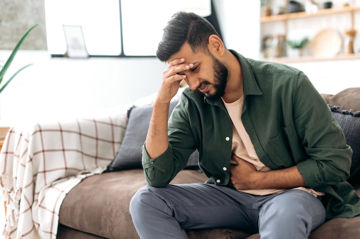 Photo un homme indien ou arabe malheureux est assis sur un canapé confortable dans un salon confortable tient ses mains sur son estomac grimaces de douleur à l'estomac souffre de spasmes d'empoisonnement problèmes d'estomac