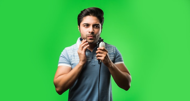 Homme indien ou asiatique rasant la barbe avec une tondeuse électrique ou une tondeuse debout isolée