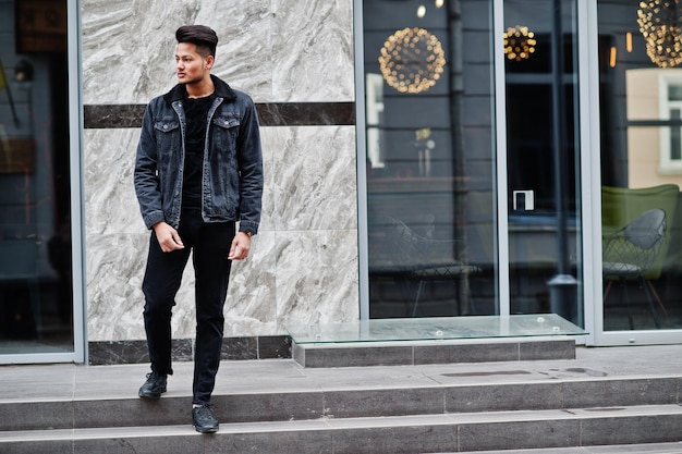 Homme indien beau et à la mode en veste de jeans noir posé en plein air