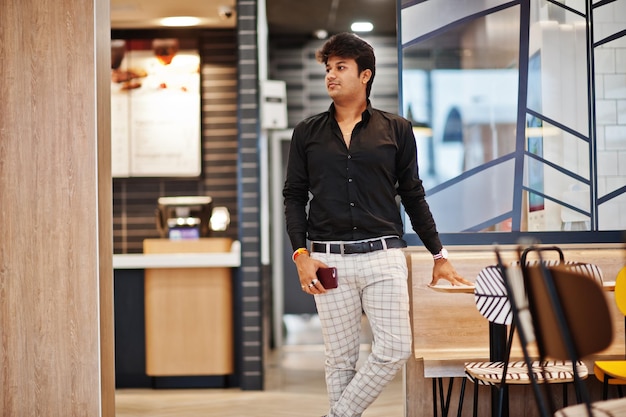 Homme indien élégant posé au café de restauration rapide avec téléphone portable à portée de main