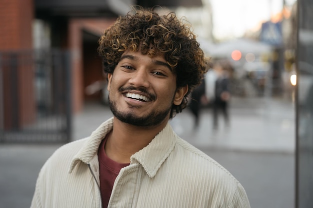 Photo homme indien élégant souriant portant des vêtements décontractés regardant la caméra dans la rue