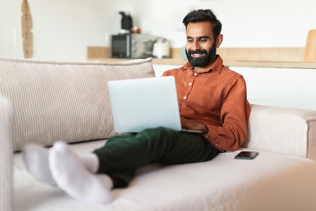 Un homme indien heureux travaillant en tant qu'indépendant en utilisant un ordinateur portable à la maison