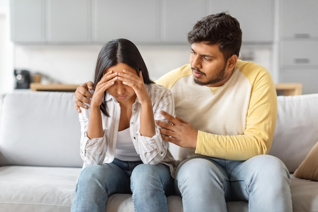 Un homme indien réconforte une femme contrariée assise sur le canapé à la maison.