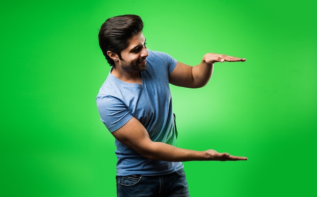 Homme indien satisfait présentant, pointant, affichant ou faisant de la publicité avec les mains ou les doigts vides. debout isolé