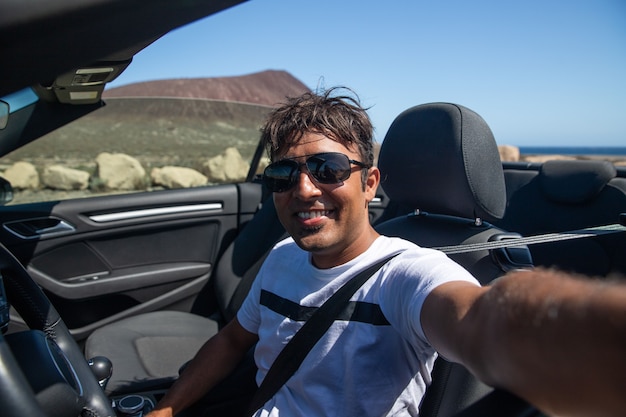 homme indien souriant assis dans sa voiture décapotable prend un selfie il est souriant et heureux