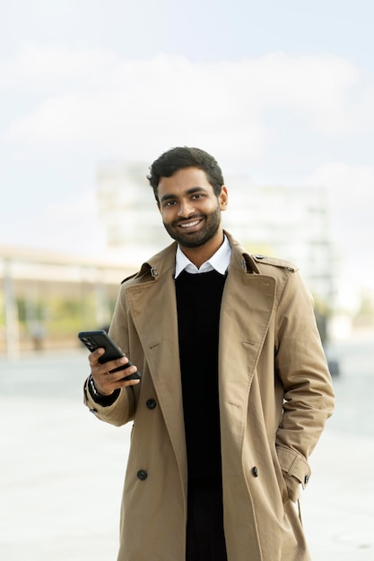 Homme indien souriant tenant un smartphone, utilisant la communication d'applications mobiles dans la rue, espace de copie