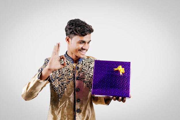 Homme indien tenant des boîtes-cadeaux surprises et une assiette vide sur DIWALI ou mariage ou festivals tout en portant des vêtements traditionnels isolés sur fond blanc