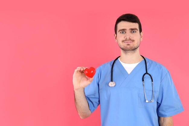L'homme d'infirmière tient le coeur rouge sur le fond rose