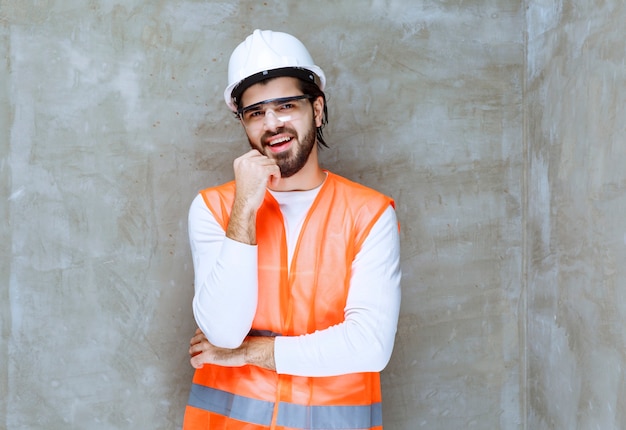 L'homme ingénieur en casque blanc et lunettes de protection a l'air confus et réfléchi.