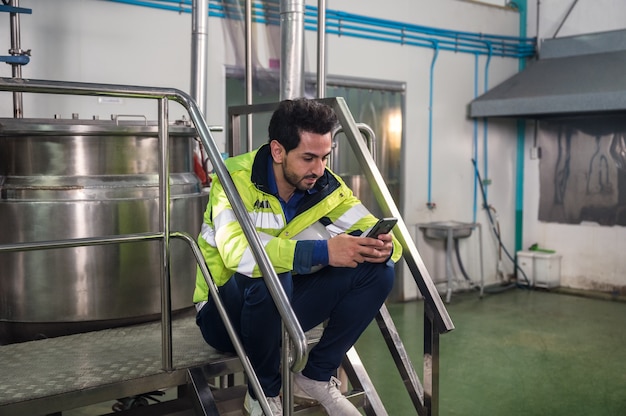 Homme ingénieur caucasien utilisant un smartphone pendant la pause dans l'escalier à l'usine de transformation des boissons