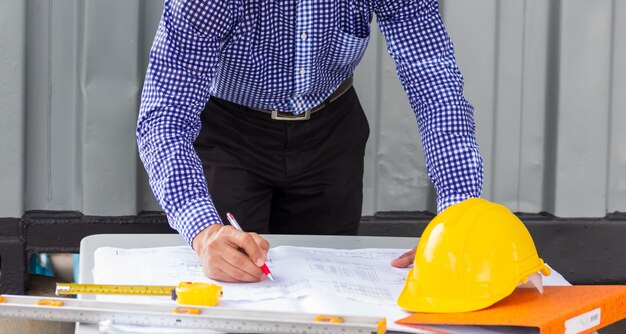 Homme ingénieur regardant le plan de projet de plan papier près du conteneur sur le chantier de construction. Travailler à l'extérieur pour voir l'avancement du nouveau projet de construction.