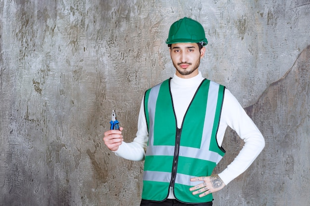 Homme ingénieur en uniforme jaune et casque tenant une pince bleue pour réparation.