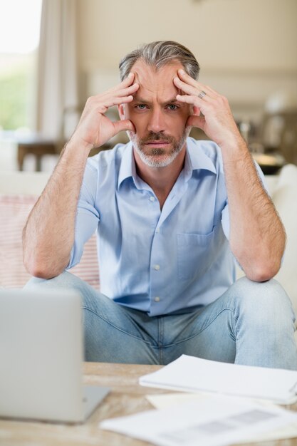 Homme inquiet assis sur un canapé avec factures et ordinateur portable dans le salon