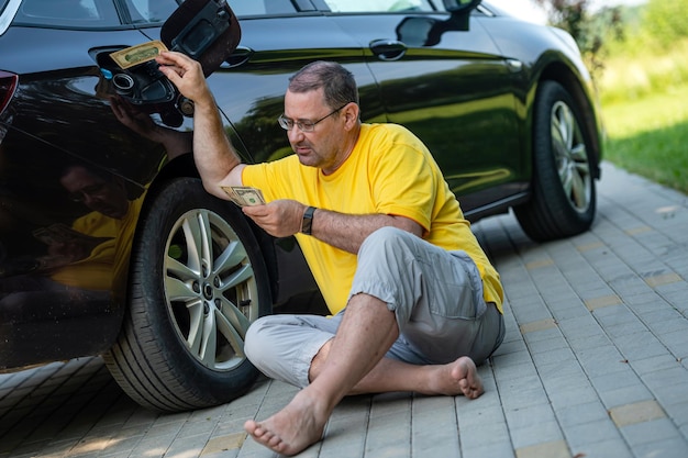 Homme inquiet assis sur le trottoir à côté d'une voiture près d'un concept de hausse des prix du carburant du réservoir de carburant ouvert