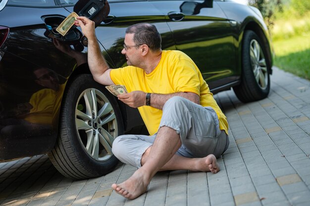 Homme inquiet assis sur le trottoir à côté d'une voiture près d'un concept de hausse des prix du carburant du réservoir de carburant ouvert