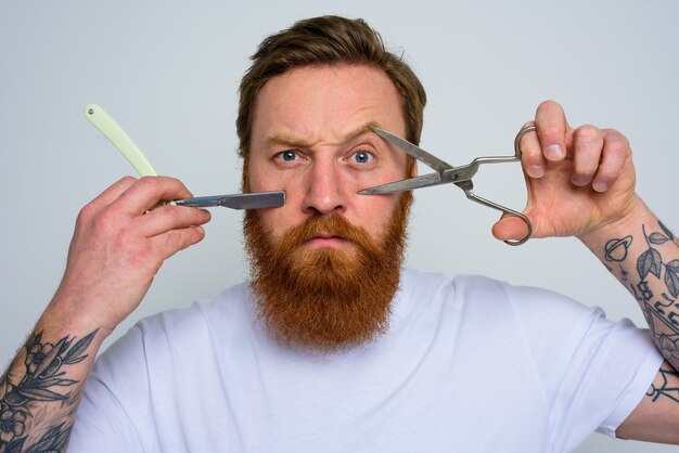 L'homme inquiet avec des ciseaux et une lame est prêt à couper la barbe