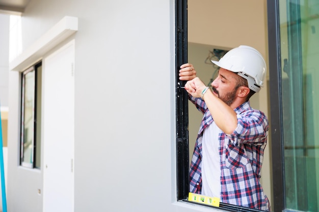 Homme installant des fenêtres dans un nouveau site de construction de maison Travailleur de la construction hispanique portant des gants de protection et un casque de protection