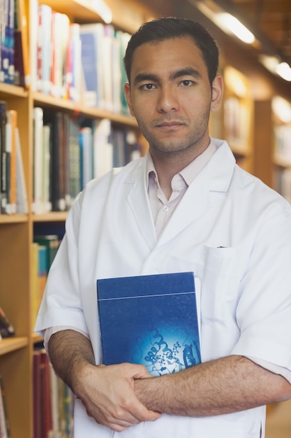 Homme intellectuel sérieux posant dans la bibliothèque avec un livre