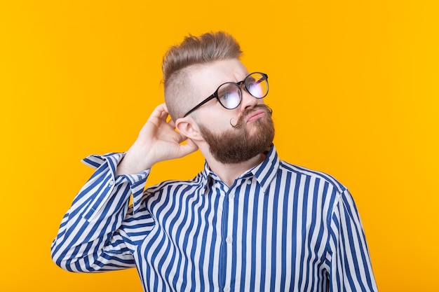 Homme intelligent mignon avec barbe posant sur un mur jaune