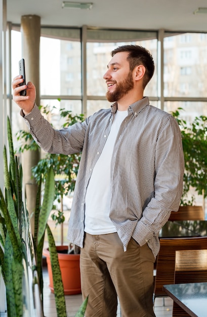 Un homme intelligent souriant a une conversation téléphonique par appel vidéo dans un bureau ou un café moderne urbain.