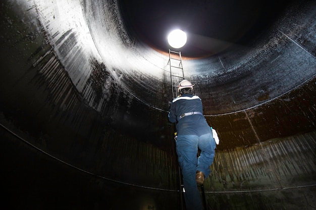 Homme à l'intérieur monter l'escalier de stockage de mazout lourd inspection visuelle du réservoir dans l'espace confiné