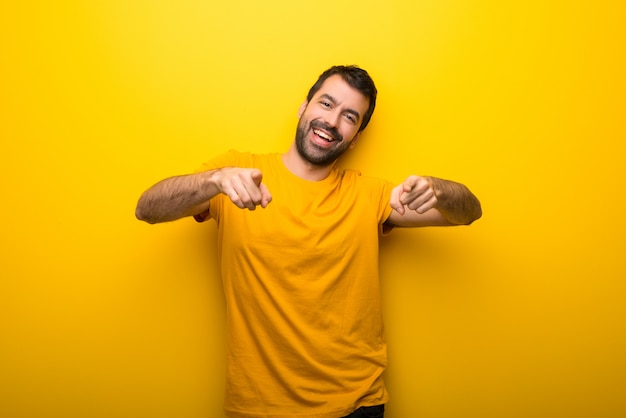 Un homme isolé sur une couleur jaune vif pointe le doigt sur vous en souriant