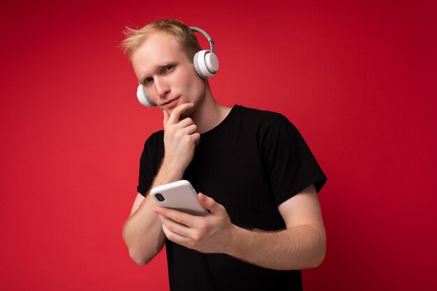 homme isolé sur le mur portant des vêtements de tous les jours tenant et utilisant un téléphone mobile écrivant des sms et pensant.