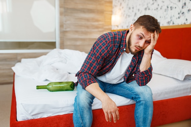 Homme ivre réveillé dans son lit avec une bouteille de vin.