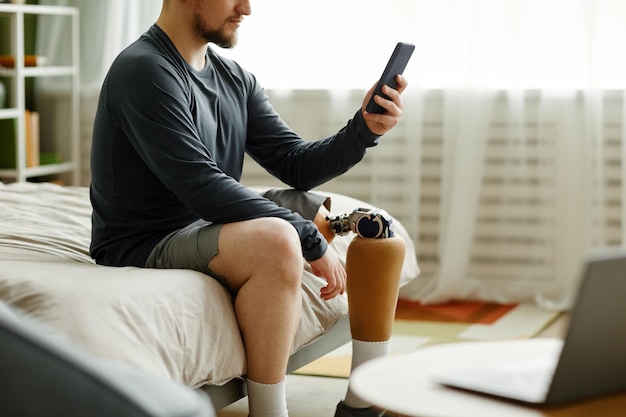Homme avec jambe prothétique utilisant un smartphone à la maison