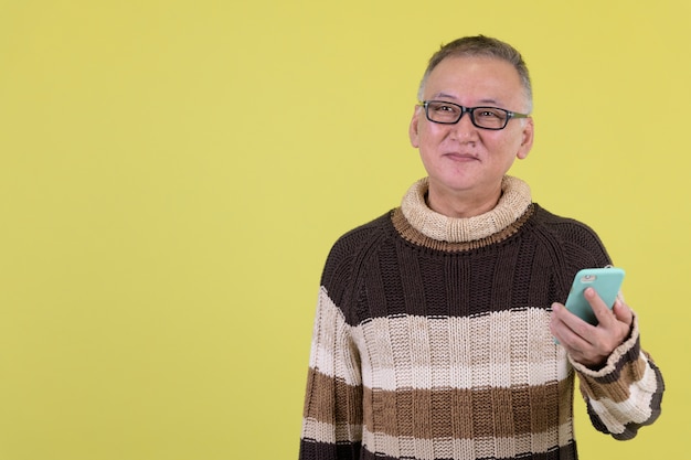 Homme japonais mature avec pull à col roulé prêt pour l'hiver contre chroma key avec mur vert