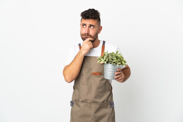 Homme jardinier tenant une plante sur fond blanc isolé ayant des doutes et de la pensée