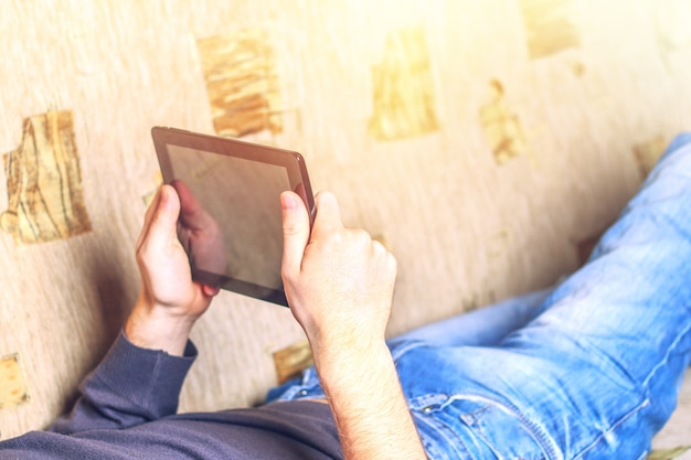 Photo homme en jeans se trouve sur le canapé et tenant une tablette.