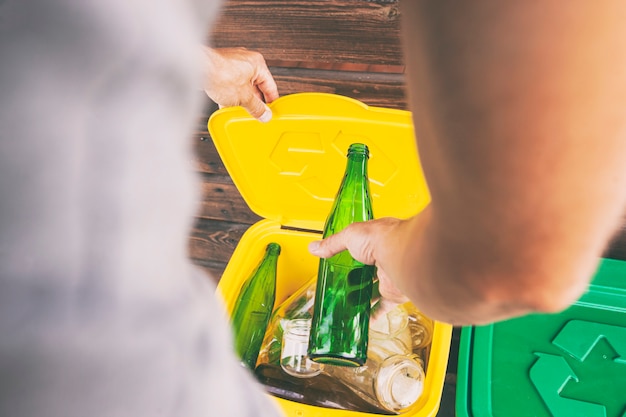 Photo homme jetant la bouteille en verre dans l'une des trois poubelles pour trier les déchets