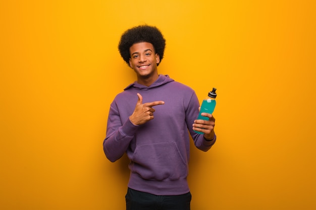 Homme jeune afro-américain de remise en forme tenant une boisson énergétique pointant vers le côté avec le doigt