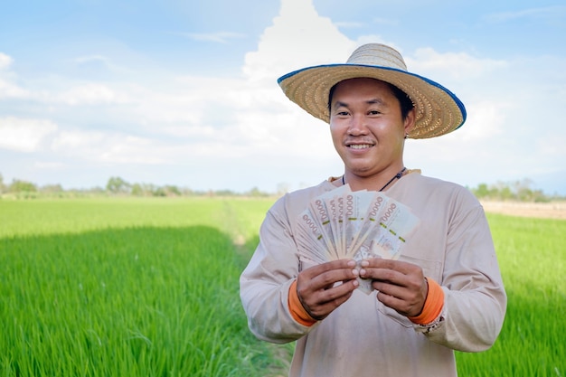 Homme jeune agriculteur asiatique tenant de l'argent de billets à la ferme de riz vert.