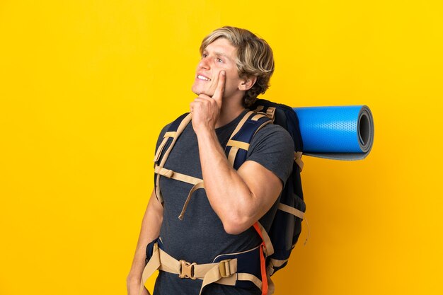 Homme jeune alpiniste sur fond jaune isolé pensant une idée tout en regardant