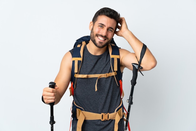 Homme jeune alpiniste avec un gros sac à dos et bâtons de randonnée isolé sur fond blanc en riant