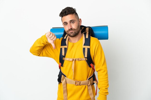 Homme jeune alpiniste avec un gros sac à dos sur fond isolé montrant le pouce vers le bas avec une expression négative